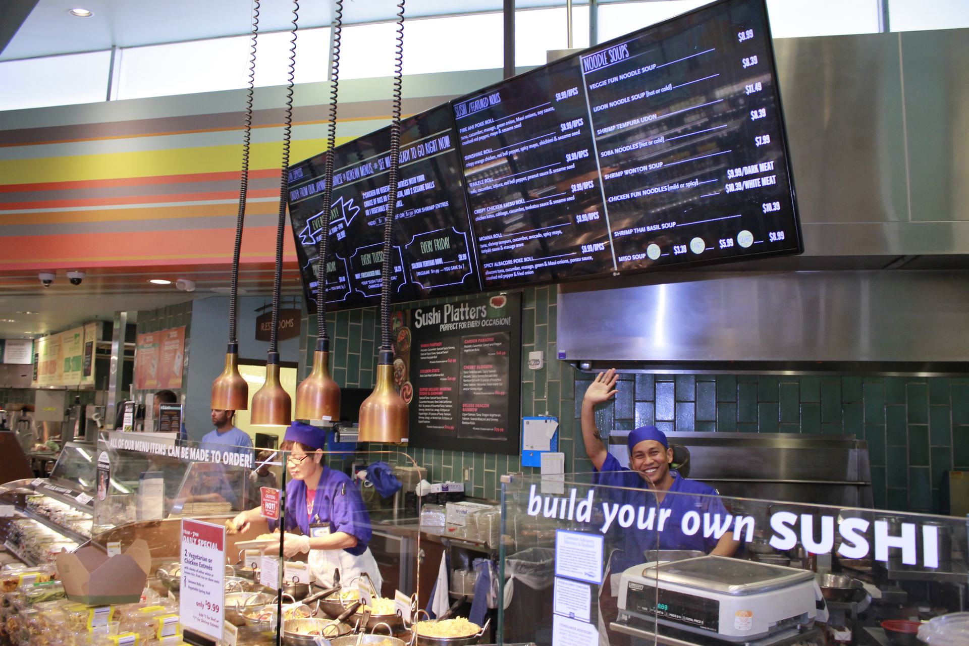 Restaurant team at a sushi counter with WAND digital menu boards overhead