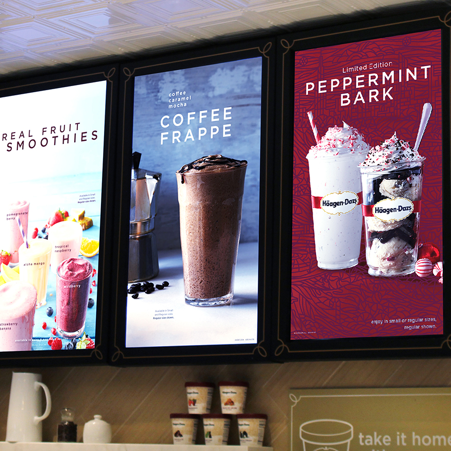 A countertop with Haagen-Dazs ice cream containers sits below five vertical digital menus showing iced coffees and smoothies.
