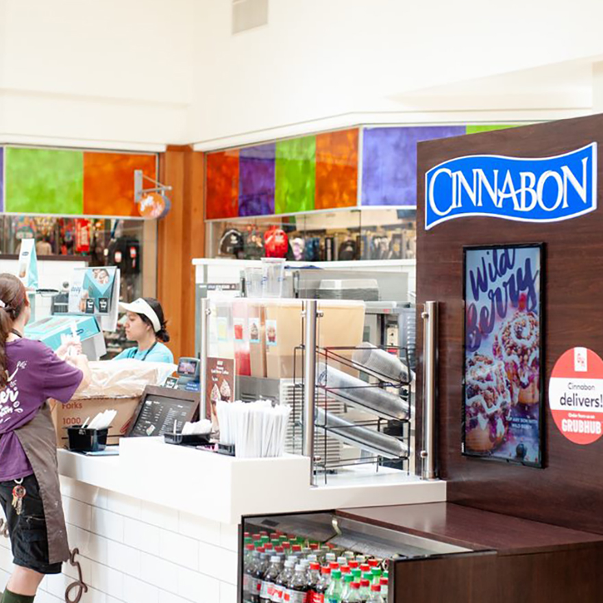 A Cinnabon storefront with customers, employees, and video menu boards hung throughout.